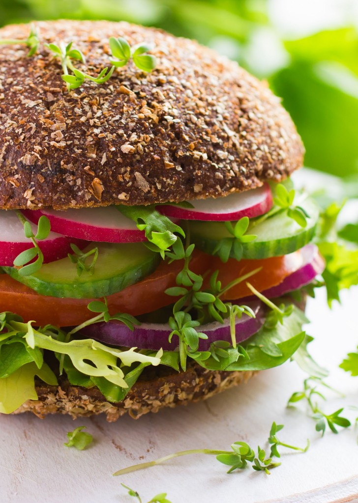 Healthy fast food. Vegan rye burger with fresh vegetables on white wooden background