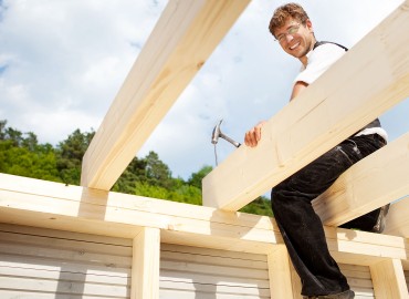 Happy carpenter sitting on the the roof beams and hammering a large nail