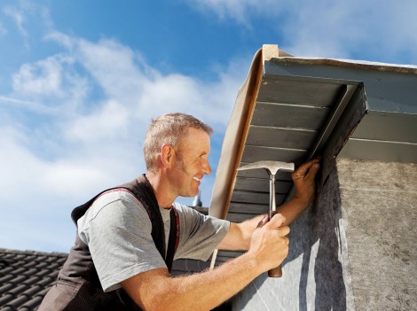 Roofer working on a new dormer by hammering nails into the roof edge