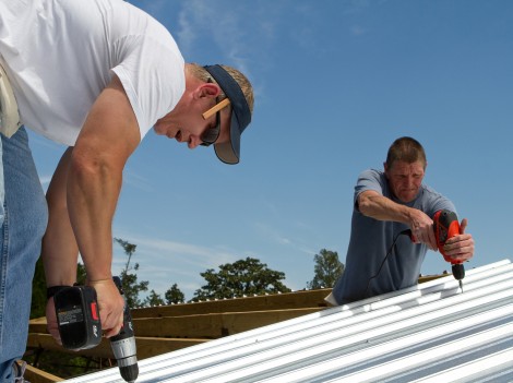Construction roofing crew uses power tools to screw and fasten sheet metal to the roof rafters of a building.