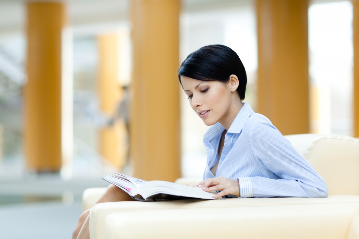 Business woman rests at the white leather sofa reading book at the hall