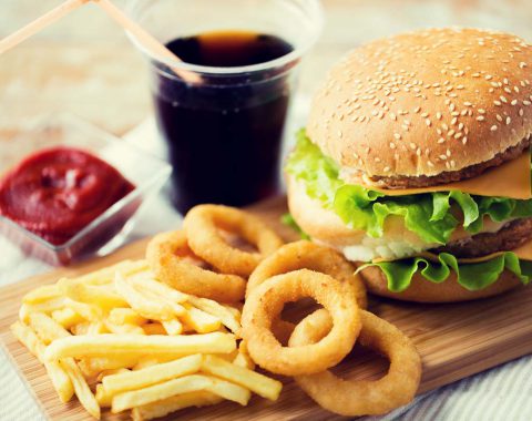 fast food and unhealthy eating concept - close up of hamburger or cheeseburger, deep-fried squid rings, french fries, coca cola drink and ketchup on wooden table