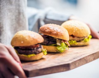 Three delicious hamburgers on wooden board. Toned image