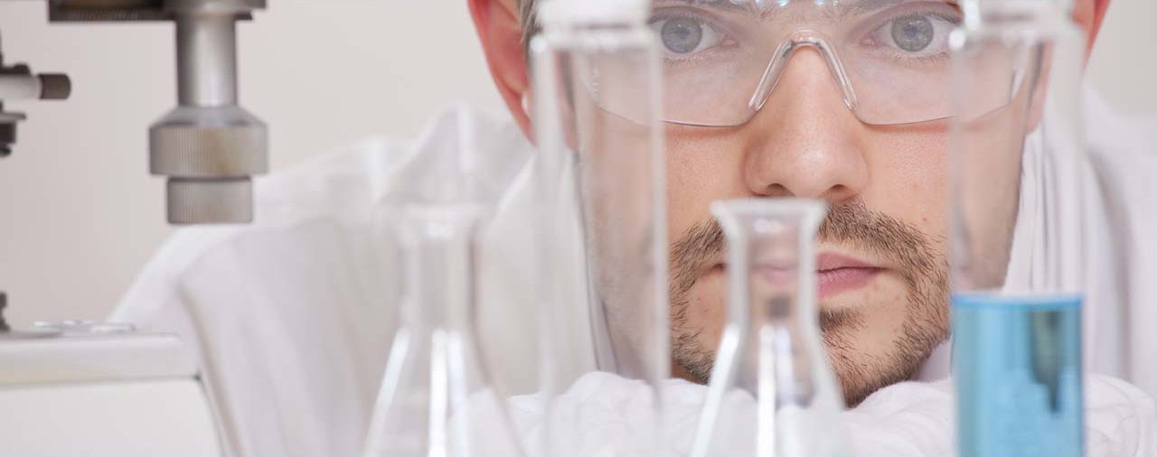 Thinking male chemical researcher with manycolourful flasks in a lab