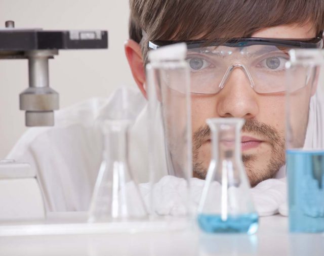 Thinking male chemical researcher with manycolourful flasks in a lab